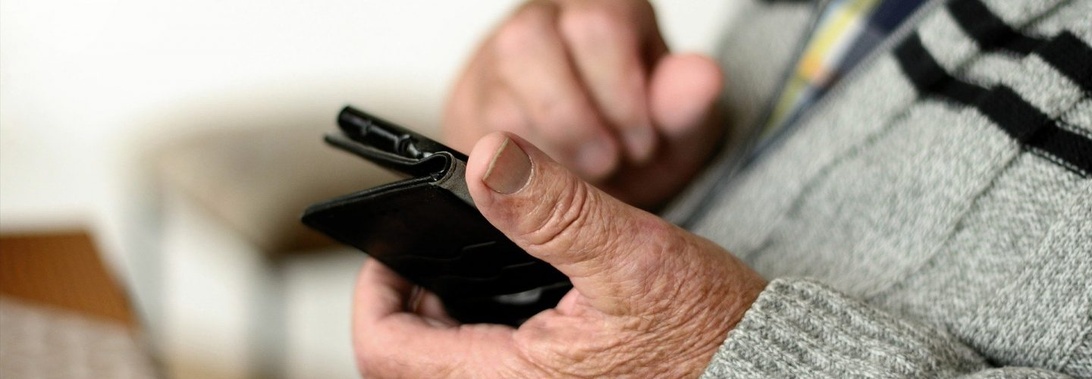 Äldre händer som håller i och använder en svart smartphone.